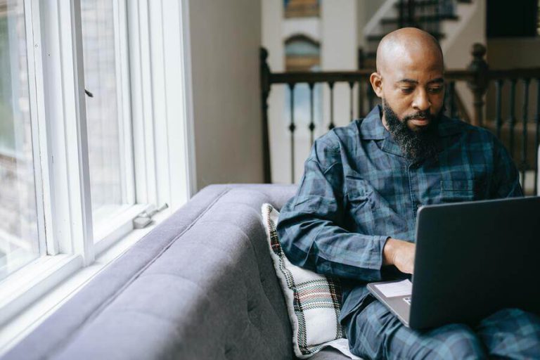 black man with beard sitting on grey couch while researching freelance business insurance.