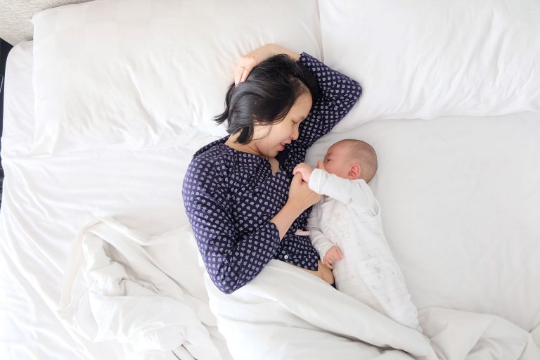 Asian mother laying in bed with infant